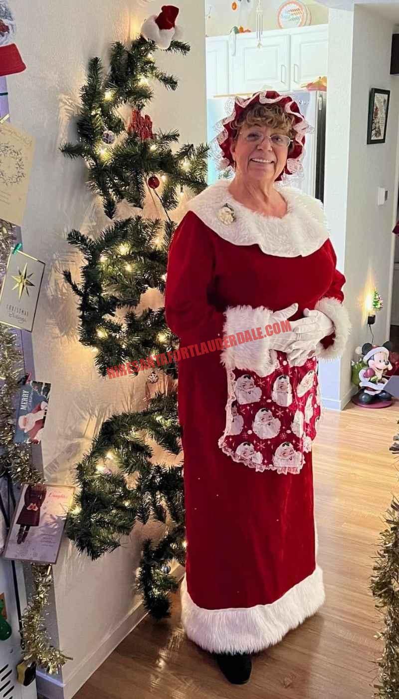 Mrs. Claus for hire in Fort Lauderdale standing beside a slim lit Christmas tree