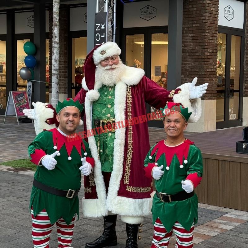 Santa Claus impersonator in Fort Lauderdale standing outdoors between two elves, burgundy coat and thumbs up