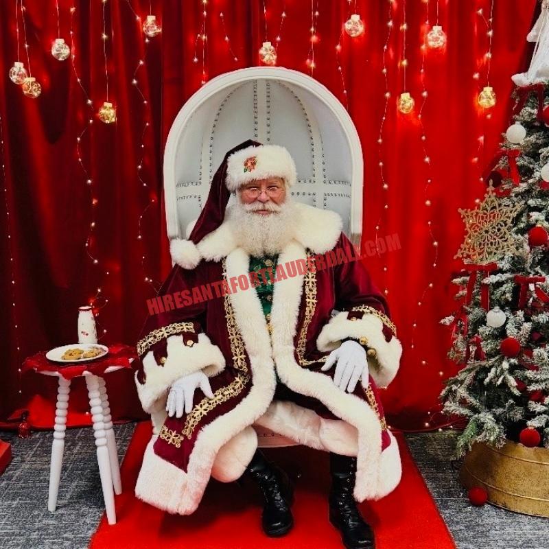 Real bearded Santa for hire in Hollywood, FL seated in a white chair with cookies and milk